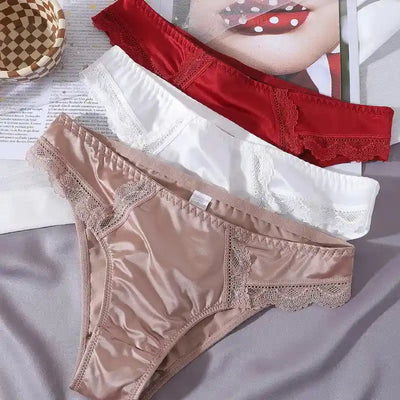 Overhead flat lay of satin panties in red, white, and nude showing lace waistband detail