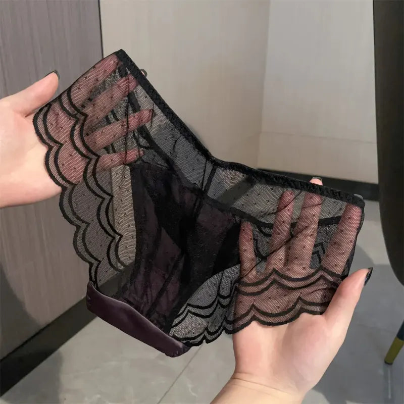 Hands holding black dot mesh scalloped satin panties showing front satin panel and ribbon bow