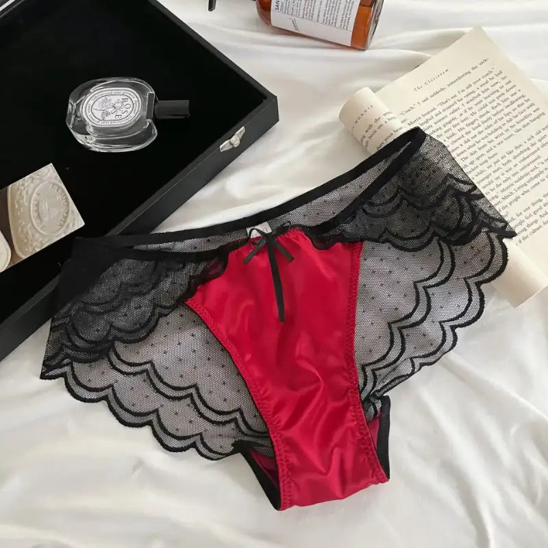 Red satin and black scalloped mesh panties with polka-dot sheer panels and ribbon bow, flat lay on white bedding