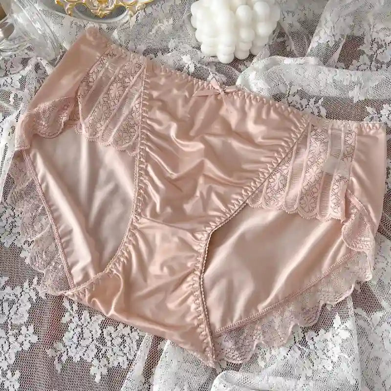 Light pink satin panties with vertical lace panels and scalloped trim, flat lay on lace fabric