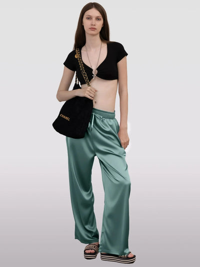 Full-length model shot of teal wide-leg satin pants with black crop top and Chanel bag