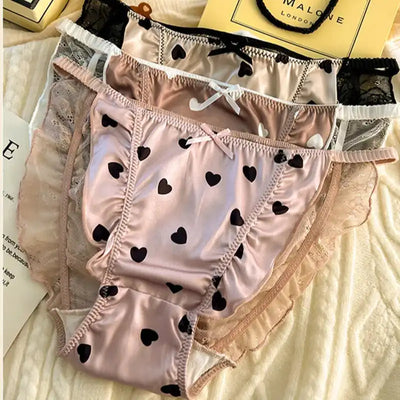 Stack of pink heart print satin panties with lace trim on white knit background