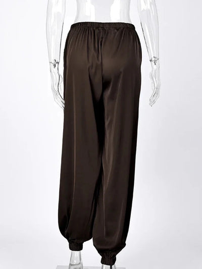 Back view of dark brown wide-leg satin pants with elastic waist and gathered ankle cuffs on mannequin