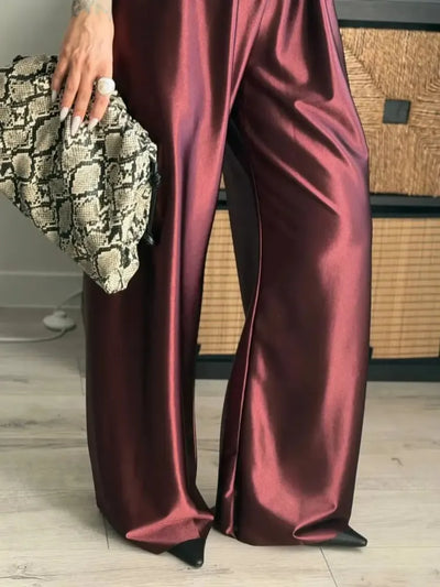 Close-up of burgundy wide-leg satin pants with a high-shine finish, held alongside a snakeskin clutch
