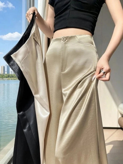 Close-up of champagne high-waisted wide-leg satin pants held open at the hip near a window