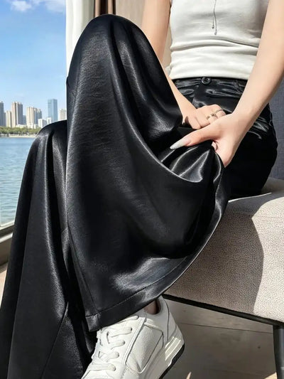 Black wide-leg satin pants held and draped over a woman's lap seated by a window