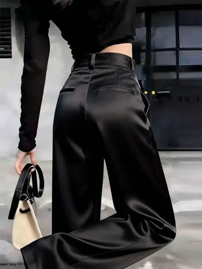 Back view of black wide-leg satin pants with high-rise waistband and welt pockets, model holding handbag