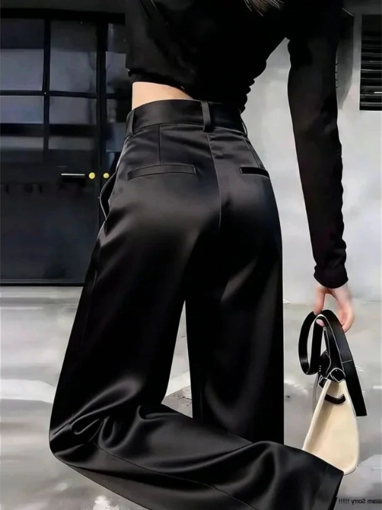 Back view of black wide-leg satin pants with high-rise waistband and welt pockets, model holding handbag