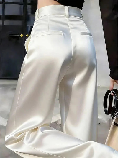 Back view of ivory wide-leg satin pants with two welt pockets and belt loops on a female model