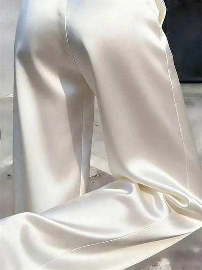 Floor-level close-up of ivory satin wide-leg pant hem pooling slightly on a concrete surface