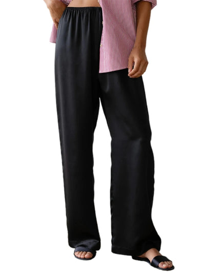 Close-up of black wide-leg satin pants with elastic waistband styled with a pink striped top and black sandals