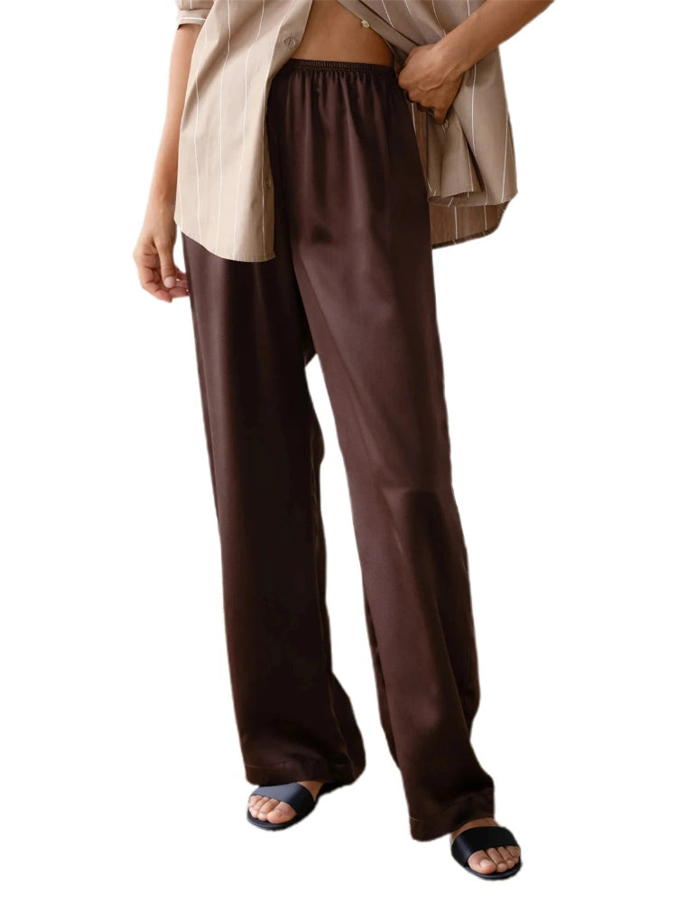 Woman wearing straight-leg chocolate brown satin pants with elastic waist and sandals