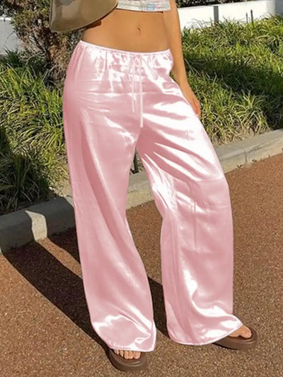 Low-rise pink wide-leg satin pants with elastic waistband worn with a cropped top and sandals