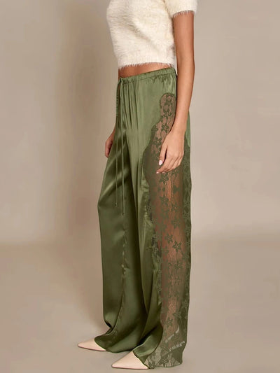 Side view of olive green wide-leg pants with sheer floral lace side panels and satin front, styled with a cream fuzzy crop top and ivory heels