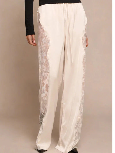 Front view of ivory wide-leg satin pants with sheer floral lace side panels and drawstring waist