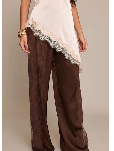 Front view of chocolate wide-leg satin pants with sheer lace side panels worn with a white lace-trim cami top