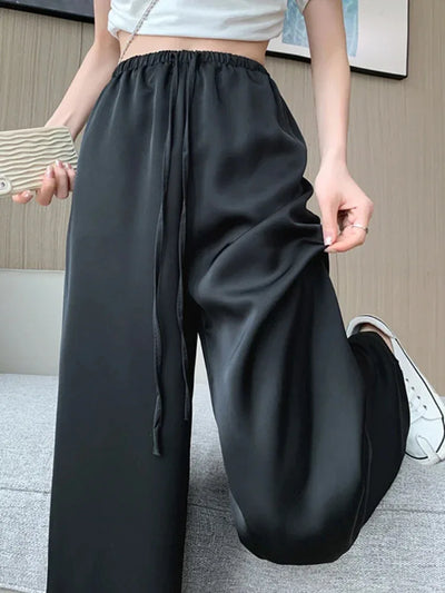 Black wide-leg satin pants with drawstring waist, held open to show fluid drape and volume