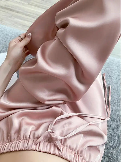 Close-up of blush satin drawstring pants held up, showing elastic waistband and fluid drape