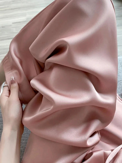 Hand gathering blush satin fabric, showing soft folds and high-shine liquid finish