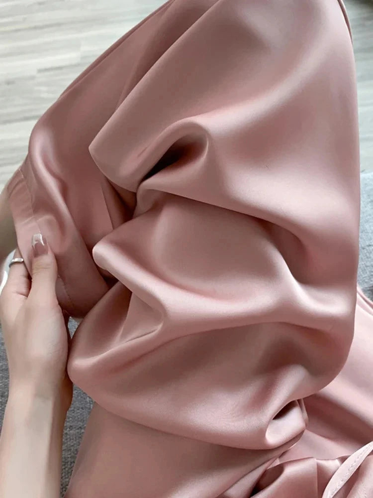 Close-up of blush satin drawstring pants held up, showing elastic waistband and fluid drape
