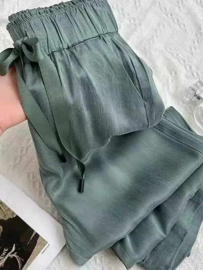 Close-up of sage green wide-leg satin pants with elastic waistband and drawstring tie detail