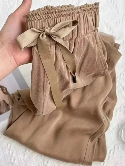 Hand holding camel high-waist pants showing satin bow-tie ribbon and elasticated waistband detail