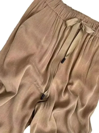 Close-up of camel satin pants waistband with tied ribbon bow and cord-tipped aglets at front