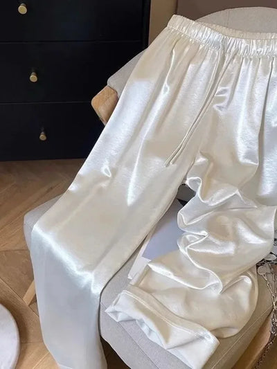 White satin wide-leg jogger pants draped over a cream armchair, drawstring waist visible