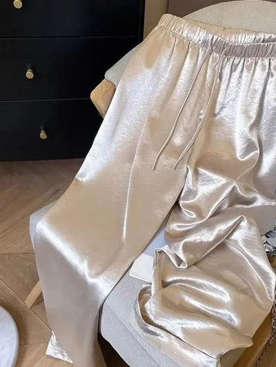 Champagne high-shine wide-leg pants draped over a cream armchair showing drawstring waist detail