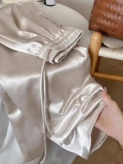 Close-up of champagne satin pants showing elasticated ankle cuffs and fluid glossy fabric held by hand