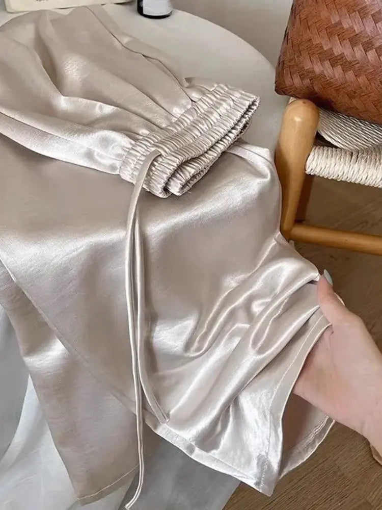 Champagne high-shine wide-leg pants draped over a cream armchair showing drawstring waist detail