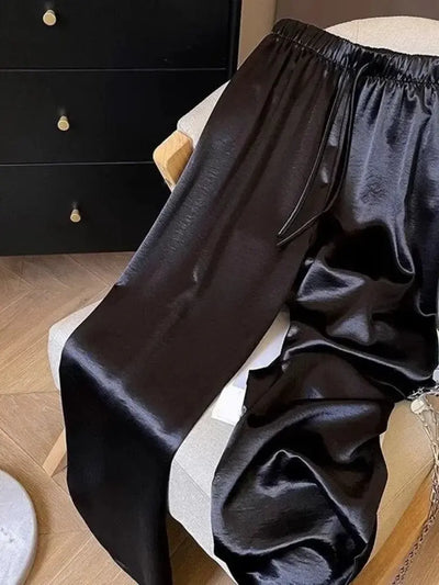 Black satin straight-leg pants with elastic waist draped over an armchair, side pocket detail visible