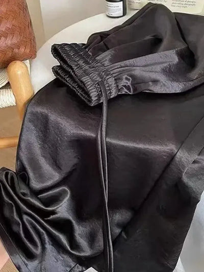 Close-up of black satin pants showing elasticated waistband with drawstring tie and fluid drape
