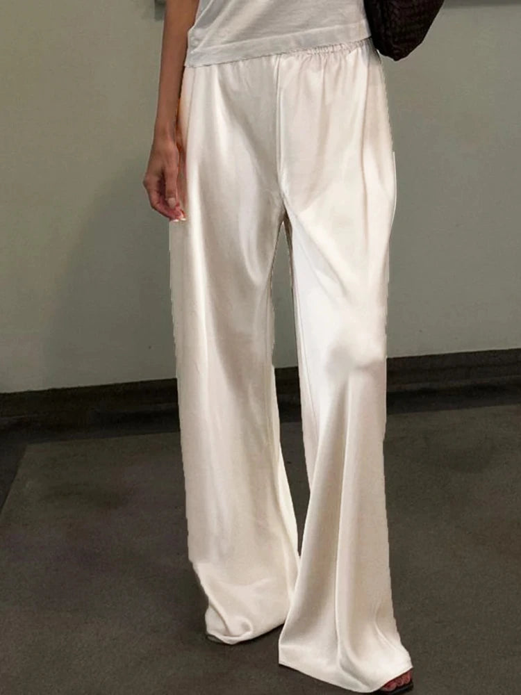 Woman wearing ivory wide-leg satin pants with elastic waist, full-length front view indoors