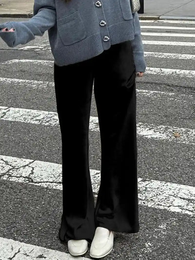 Black wide-leg satin pants styled with gray knit cardigan and white shoes on a crosswalk