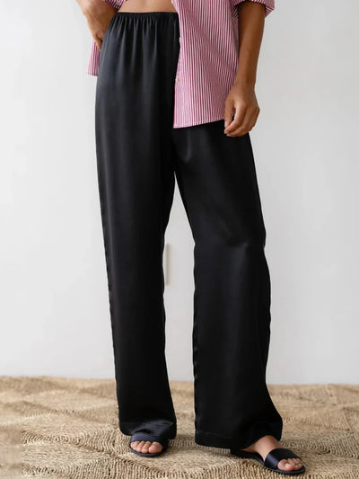 Black straight-leg satin pants with elastic waistband paired with pink striped top and black sandals