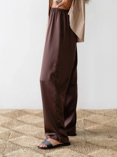Side view of chocolate wide-leg satin pants with elastic waist and slide sandals