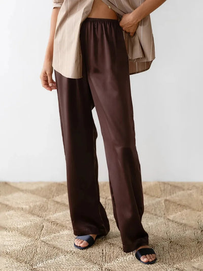 Front view of chocolate wide-leg satin pants paired with striped beige button-down shirt