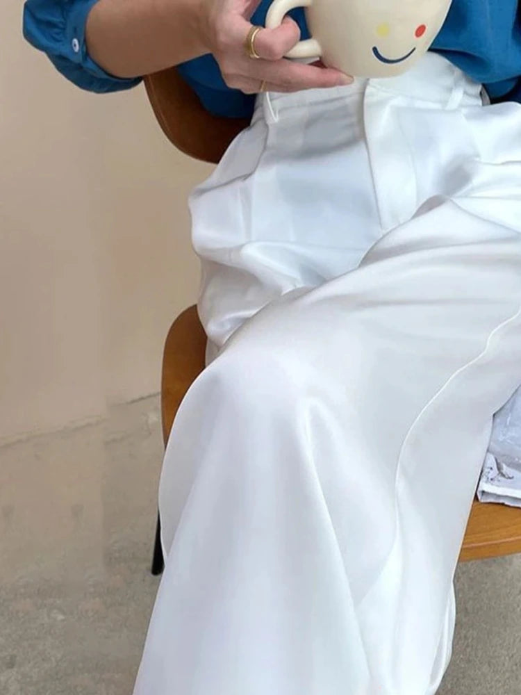 Woman seated in white high-rise wide-leg satin pants holding a smiley-face mug