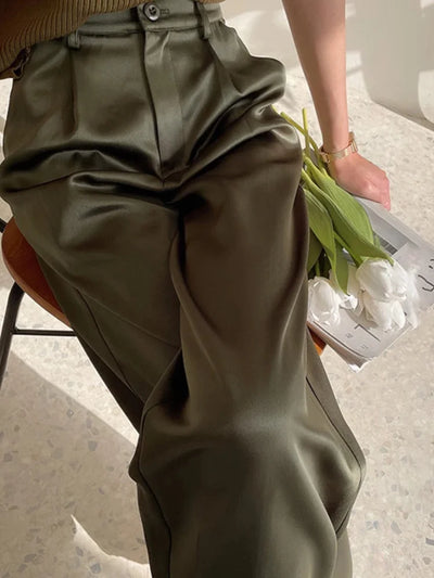 Close-up of olive pleated high-waisted wide-leg pants with button waistband detail and fluid drape