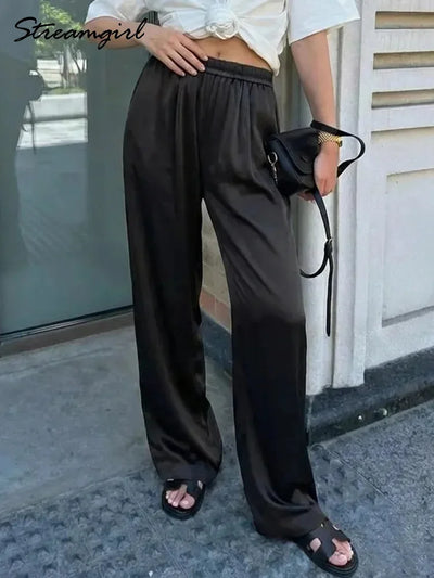 Black wide-leg satin pants with elastic waist worn with white crop top and black sandals outdoors