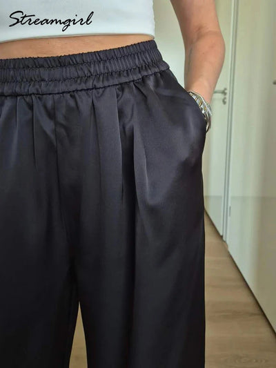 Close-up of black satin pants showing elastic smocked waistband and front pleats with side pocket