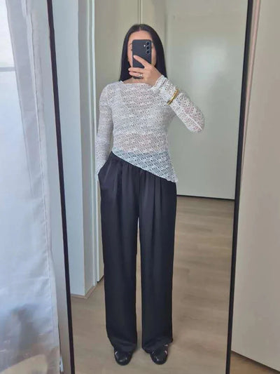 Full-length mirror shot of black wide-leg satin pants styled with a white open-knit long-sleeve top