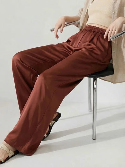Woman seated in rust wide-leg satin pants with elastic waist, styled with cream crop top and beige cardigan