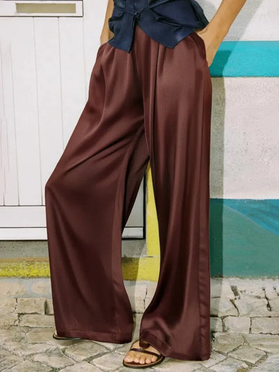 Close-up of rust wide-leg satin pants showing fluid drape and high-shine finish at floor length