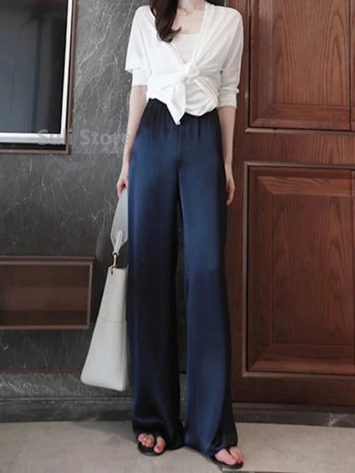 Woman standing in navy high-rise wide-leg satin pants paired with a white knotted blouse and black sandals