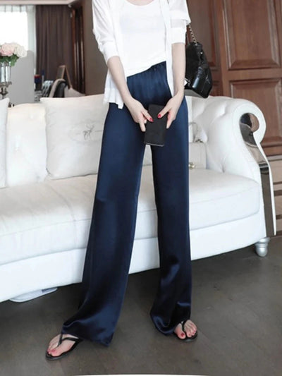Close front view of navy high-rise wide-leg pants with glossy finish styled with white open cardigan and black wallet