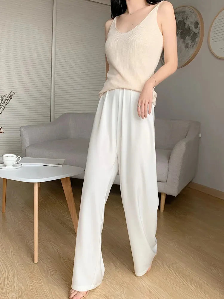 Woman wearing cream wide-leg satin pants and beige knit tank top in a modern living room