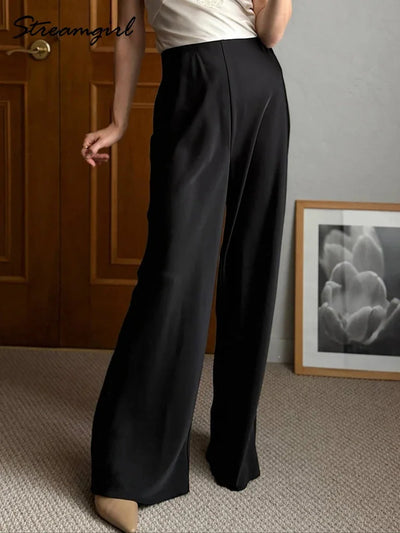 Woman wearing black high-waisted wide-leg satin pants with pointed-toe nude flats indoors