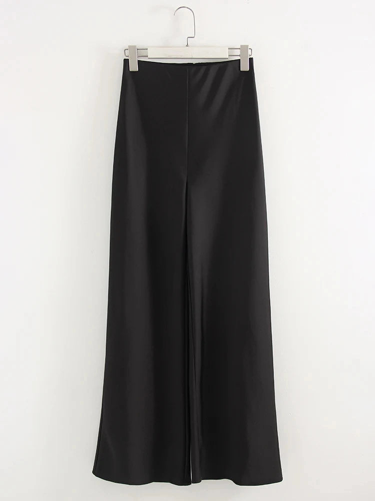 Woman wearing black high-waisted wide-leg satin pants with pointed-toe nude flats indoors